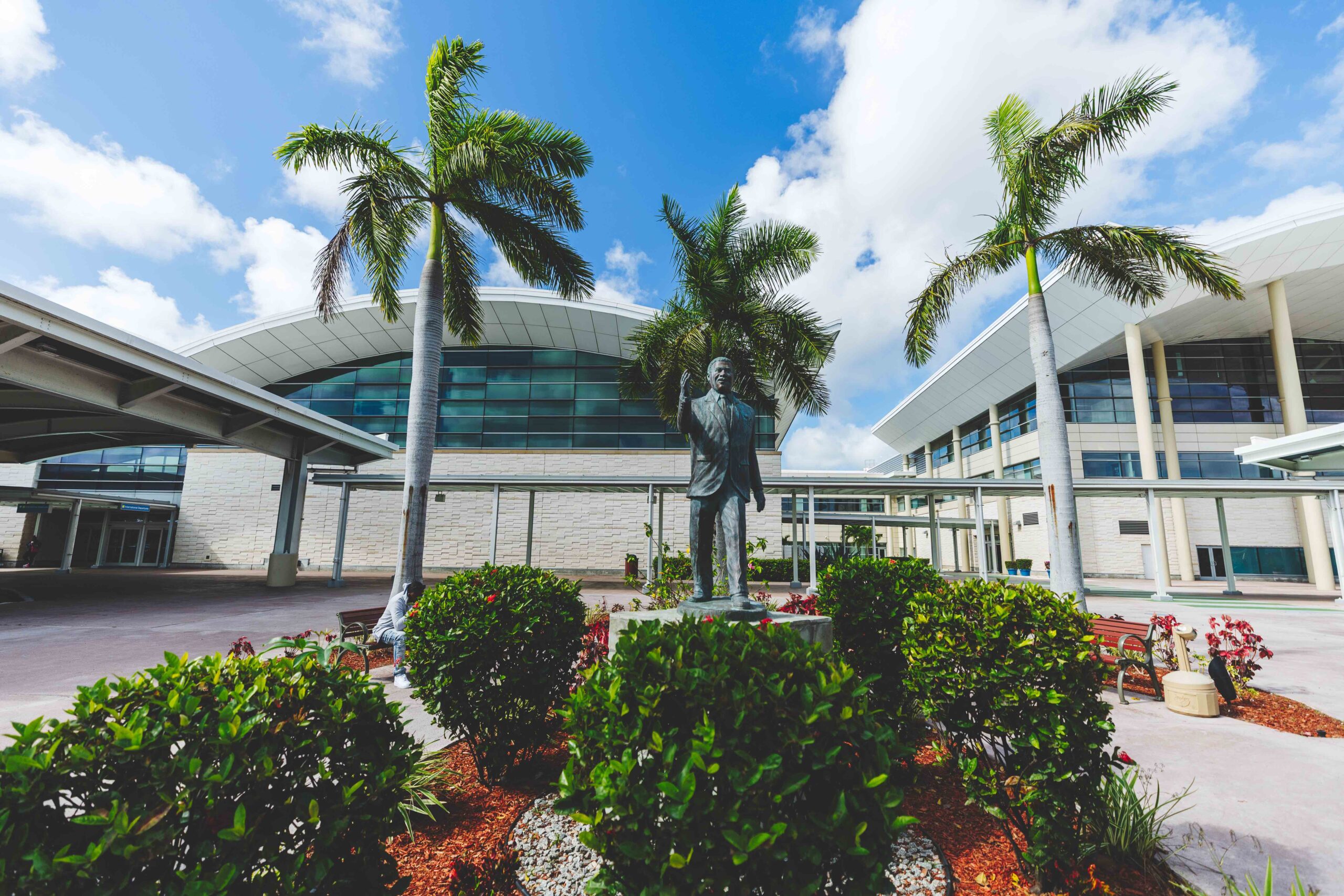 The exterior entrance of the airport with palm trees and a blue sky.